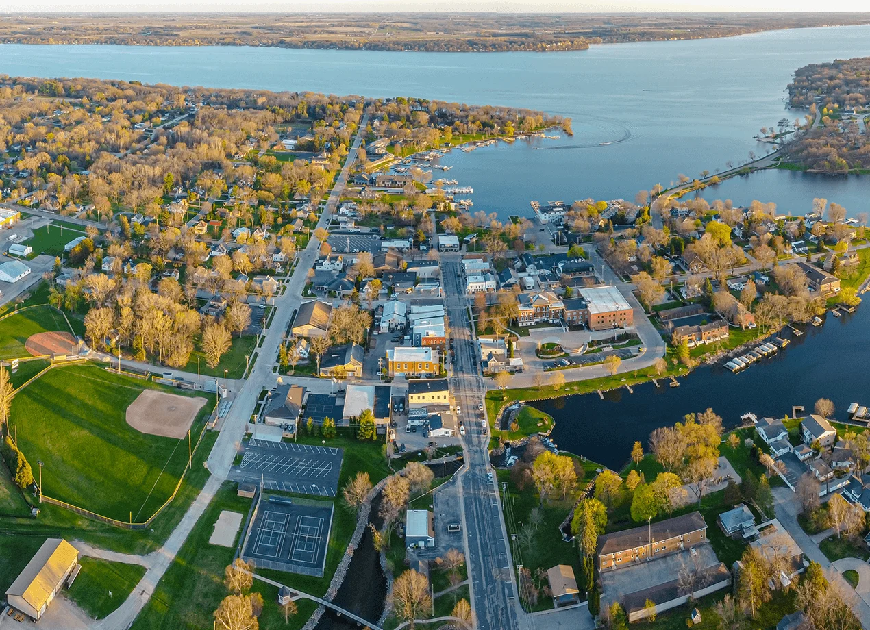 Aerial view of a scenic lakeside town, featuring green parks, sports fields, residential areas, and a bustling waterfront.