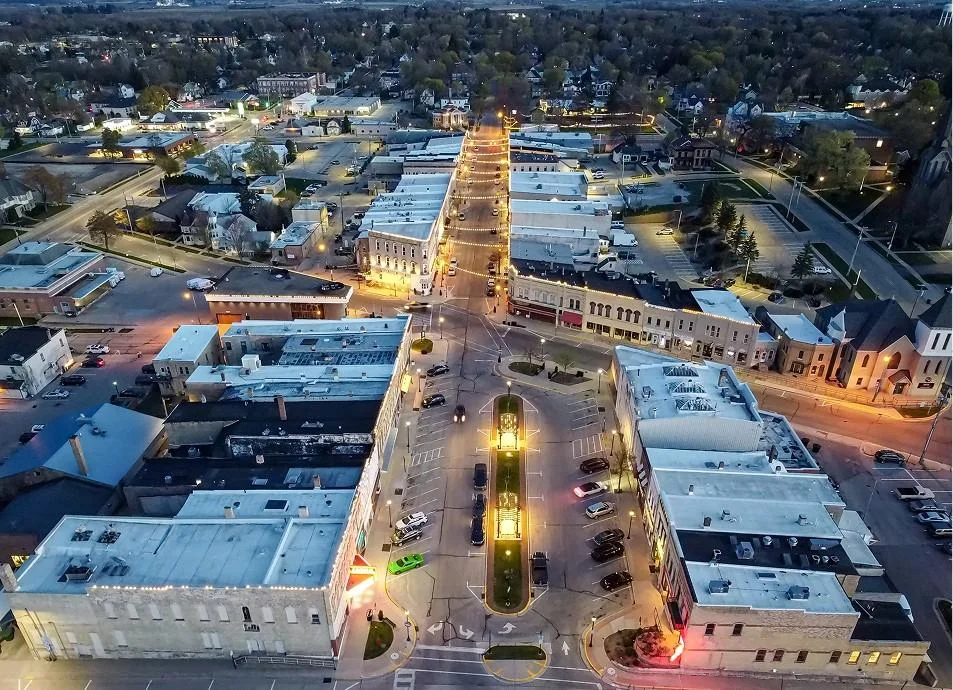 Aerial view of a town at dusk, showcasing illuminated buildings and streets under a twilight sky.