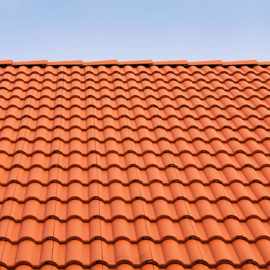 A rooftop of a house with tile shingles against a clear blue sky.