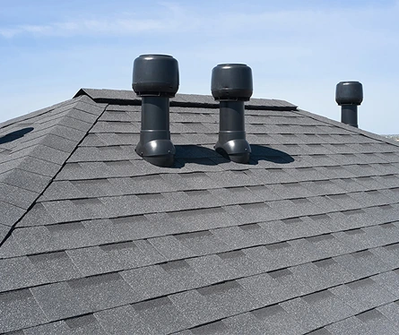 Close-up view of a rooftop with three large black ventilation pipes on gray shingles.