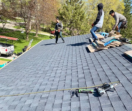 Roofers installing asphalt shingles on a residential rooftop during a sunny day