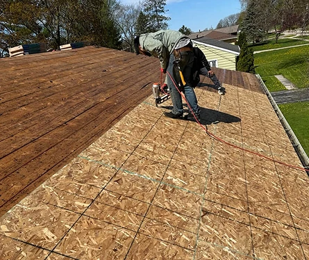 Worker using a nail gun to secure wooden decking on a roof under construction