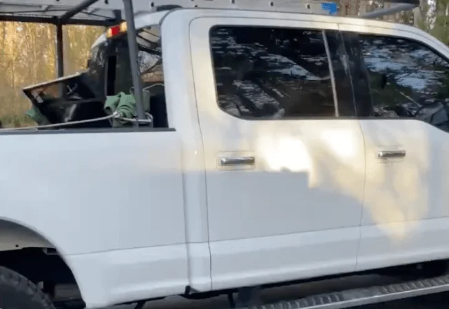 A white truck parked outdoors, featuring a ladder attached to its side.