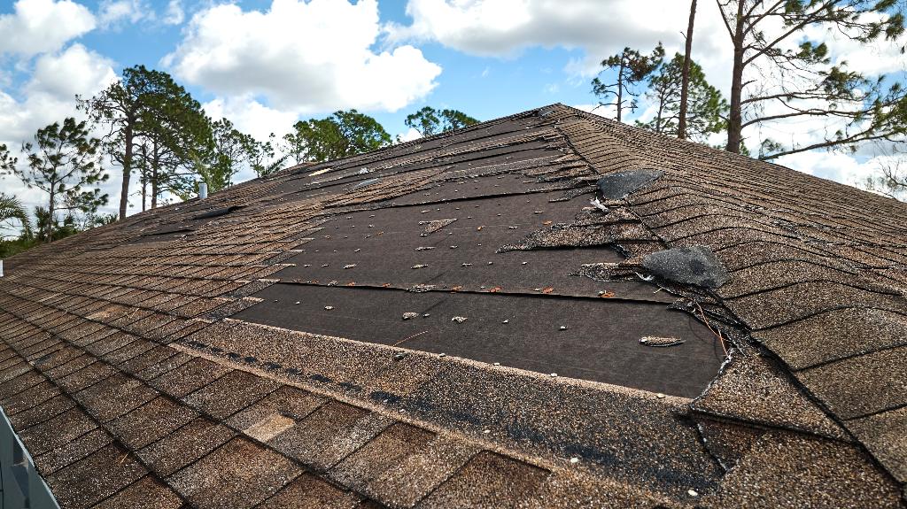 damaged house roof with missing asphalt shingles