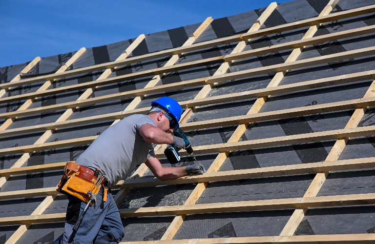Construction worker in protective clothing standing on roof with tools