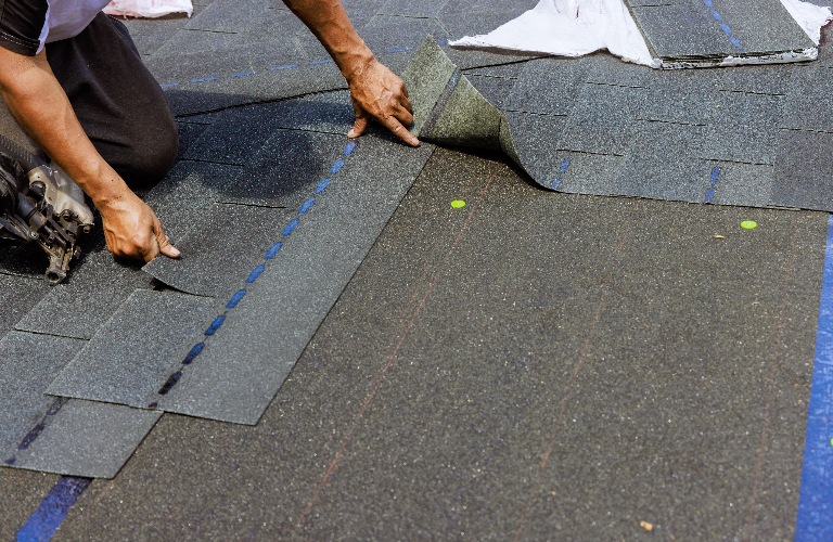 Construction worker installing new bitumen shingles on roof